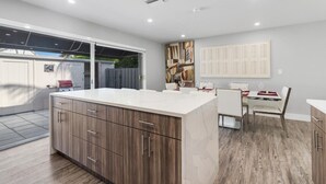 A modern kitchen with a large island, wooden cabinets, and a dining area with a table and chairs.