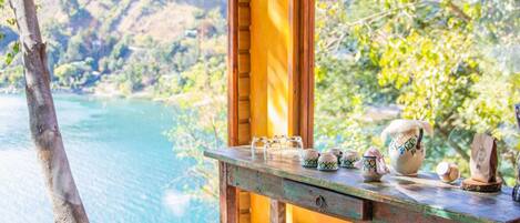 A cabin with a wooden interior, a dining table with kitchen appliances, and a view of a lake and mountains.