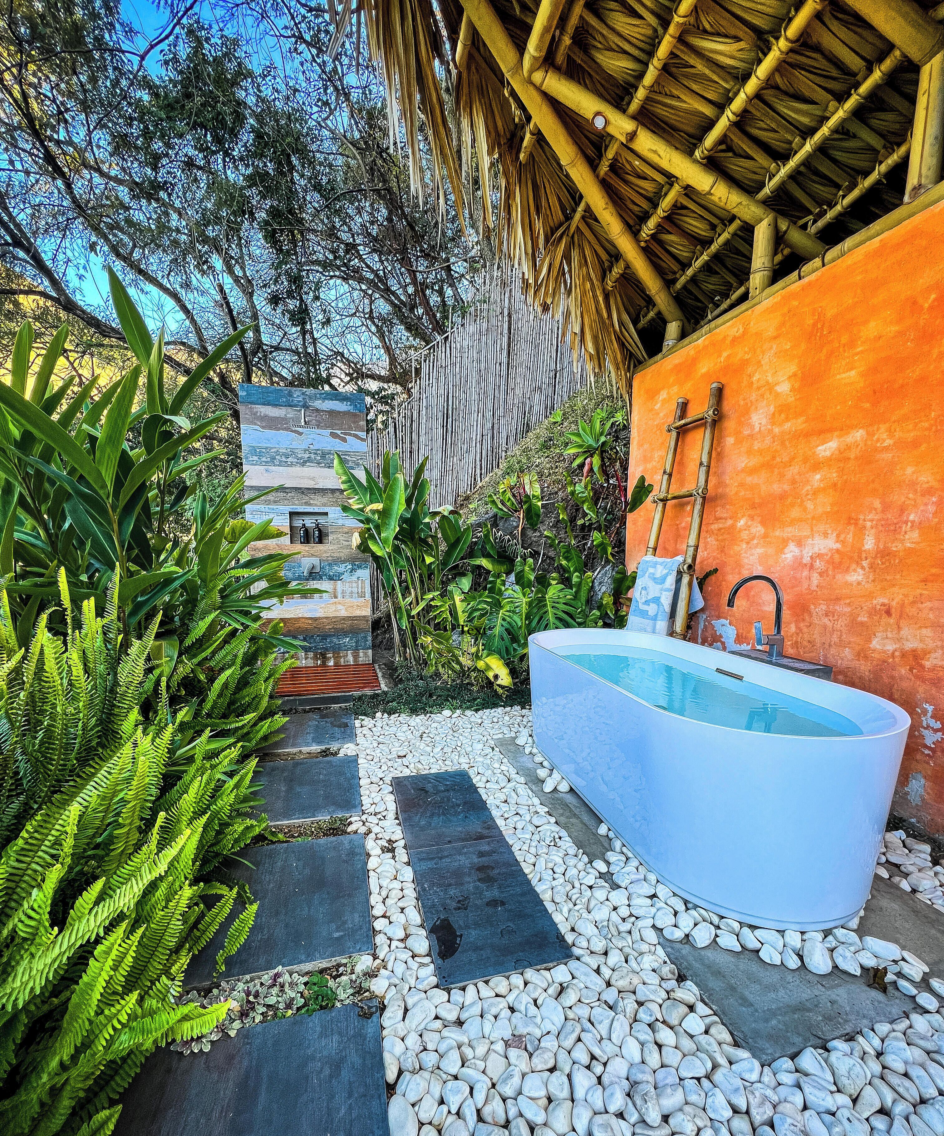 Un'area piscina moderna all'aperto con vialetto in pietra, una vasca da bagno ampia e bianca, e rigogliosa vegetazione.