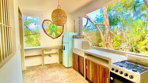 A kitchen with a gas stove, a refrigerator, and a window with a view of trees. - El Eden Escondido (Puerto Escondido)