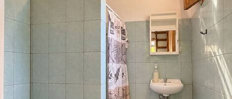 A bathroom with a shower, toilet, sink, and a ceiling with wooden beams.