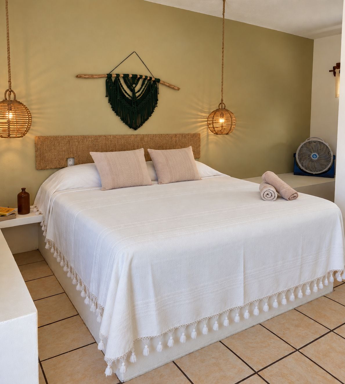 A neatly made bed with a white bedspread and pillows, a woven headboard, and two hanging wicker lamps.