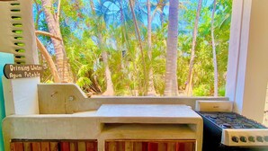 A kitchen with a view of a tropical forest, a stove, and a sign indicating a drinking water source. - El Eden Escondido (Puerto Escondido)