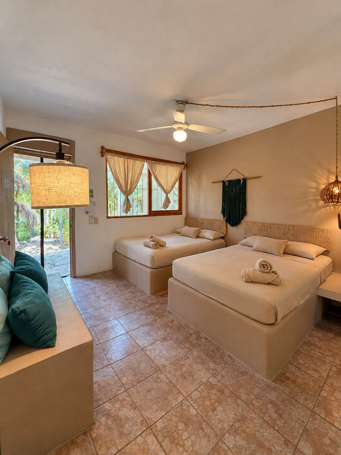 Una habitación con dos camas, ventilador de techo, ventana con cortinas e iluminación empotrada en la pared.