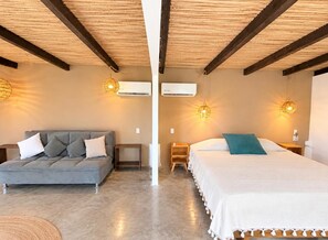 A room with a grey sofa, a bed with a white and teal pillow, wooden beams on the ceiling, and two wall-mounted air conditioners. - El Eden Escondido (Puerto Escondido)