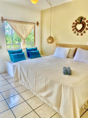 A neatly made bed with white and blue pillows, a white bedspread, and rolled towels on the bed. - El Eden Escondido (Puerto Escondido)