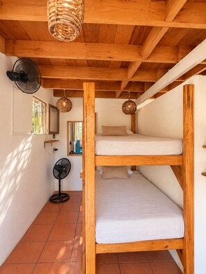 A small, cozy room with a bunk bed, a standing fan, and a woven light fixture. - El Eden Escondido (Puerto Escondido)