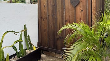 Una puerta de madera con un recorte en forma de corazón, suelo de hormigón y plantas en macetas, incluyendo una palmera.