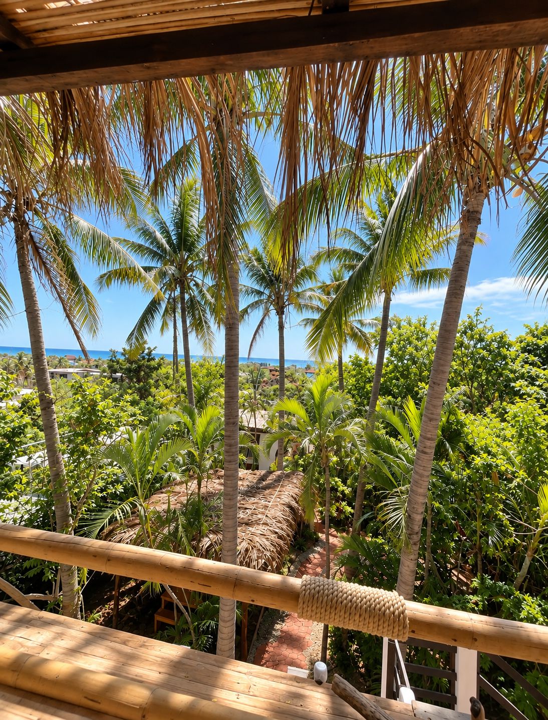 A wooden deck overlooking a tropical garden with palm trees and a clear view of the ocean.