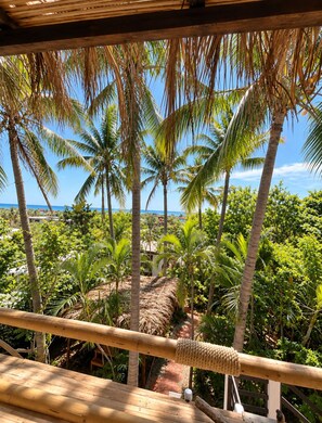 Une terrasse en bois donnant sur un jardin tropical, avec des palmiers, et offrant une vue dégagée sur l’océan.