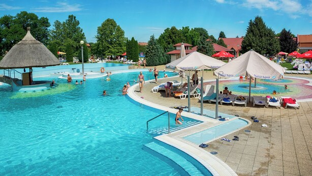 Una gran piscina exterior amb diverses línies, envoltada de gandules i ombrelles.