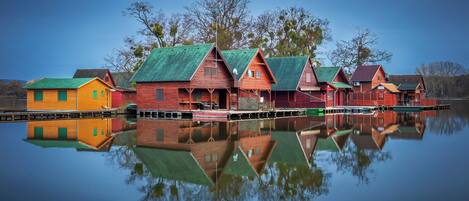 Une rangée de cabanes en bois aux toits verts, qui se reflètent sur l’eau calme.