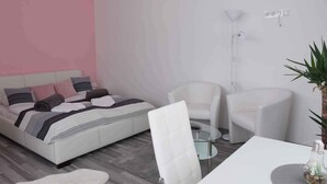 Ein modernes Schlafzimmer mit einem Bett, zwei weißen Stühlen, einem kleinen Tisch und einer Stehlampe.