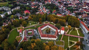 Eine Vogelperspektive zeigt eine historische Festung mit einem zentralen Innenhof, umgeben von Wohngebäuden und Grünflächen.