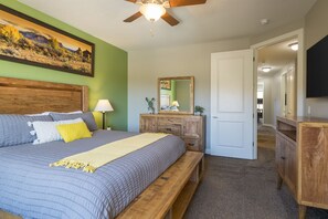 Une chambre à coucher avec un grand lit, une tête de lit en bois, un ventilateur de plafond, une table de chevet, une commode et un téléviseur.