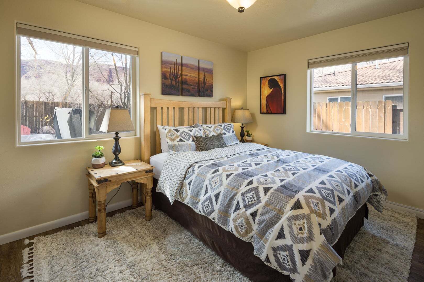A bedroom with a bed, two bedside tables, a window, and artwork on the walls.