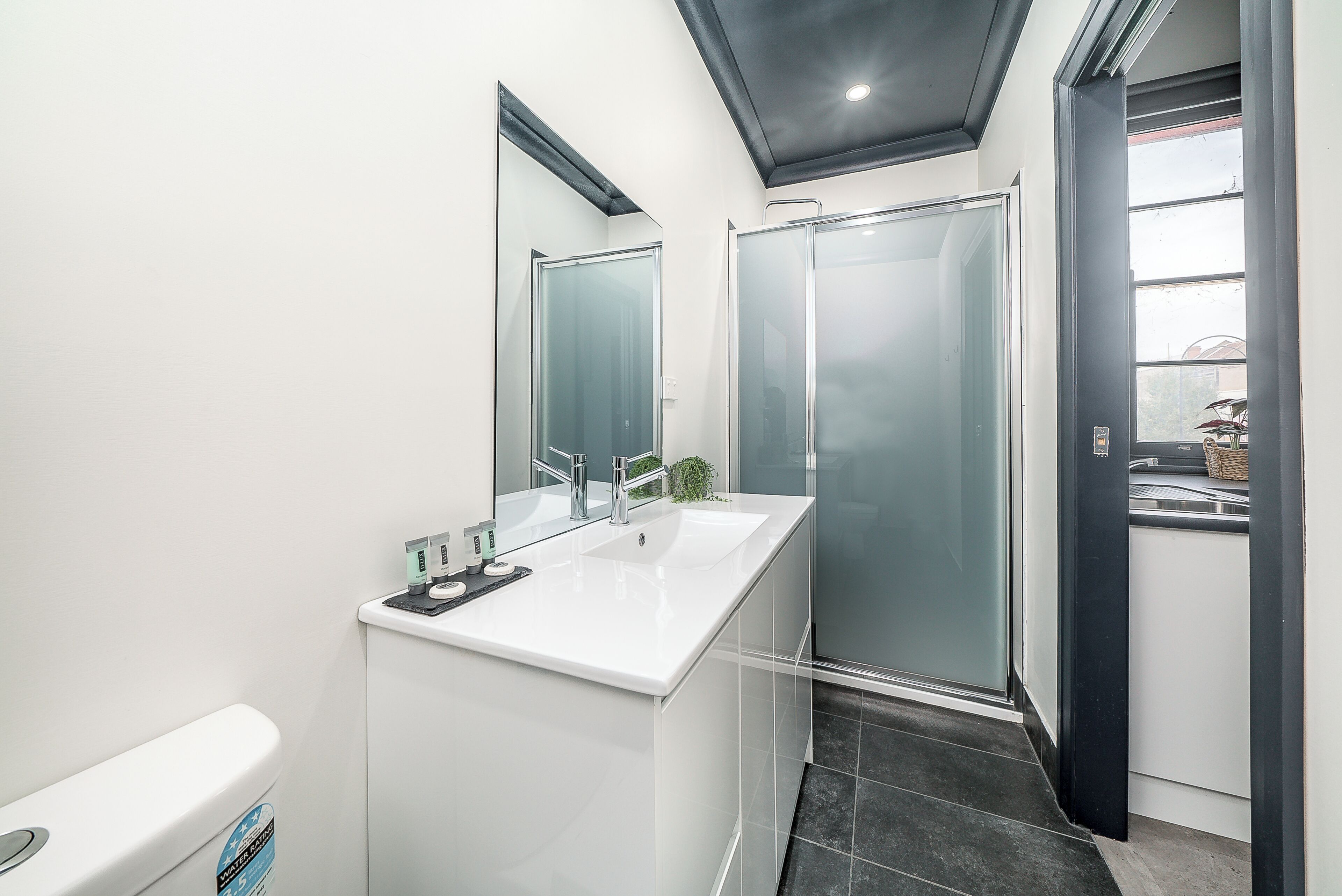 Un baño moderno con tocador blanco, cabina de ducha de vidrio y inodoro a la vista.