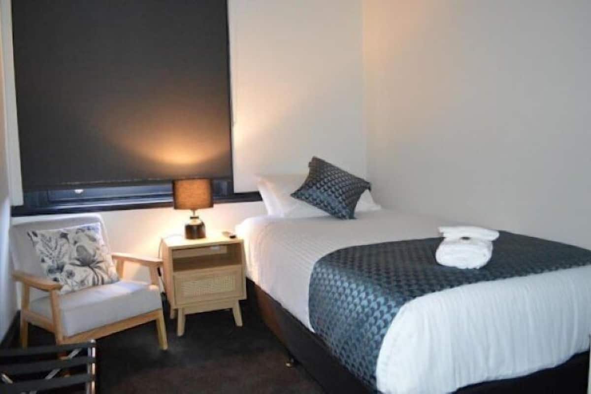 A bedroom with a bed, a chair, a nightstand, and a lamp.