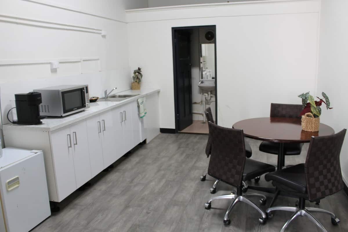 A conference room with a round table, four chairs, a coffee machine, and a microwave on a white countertop.