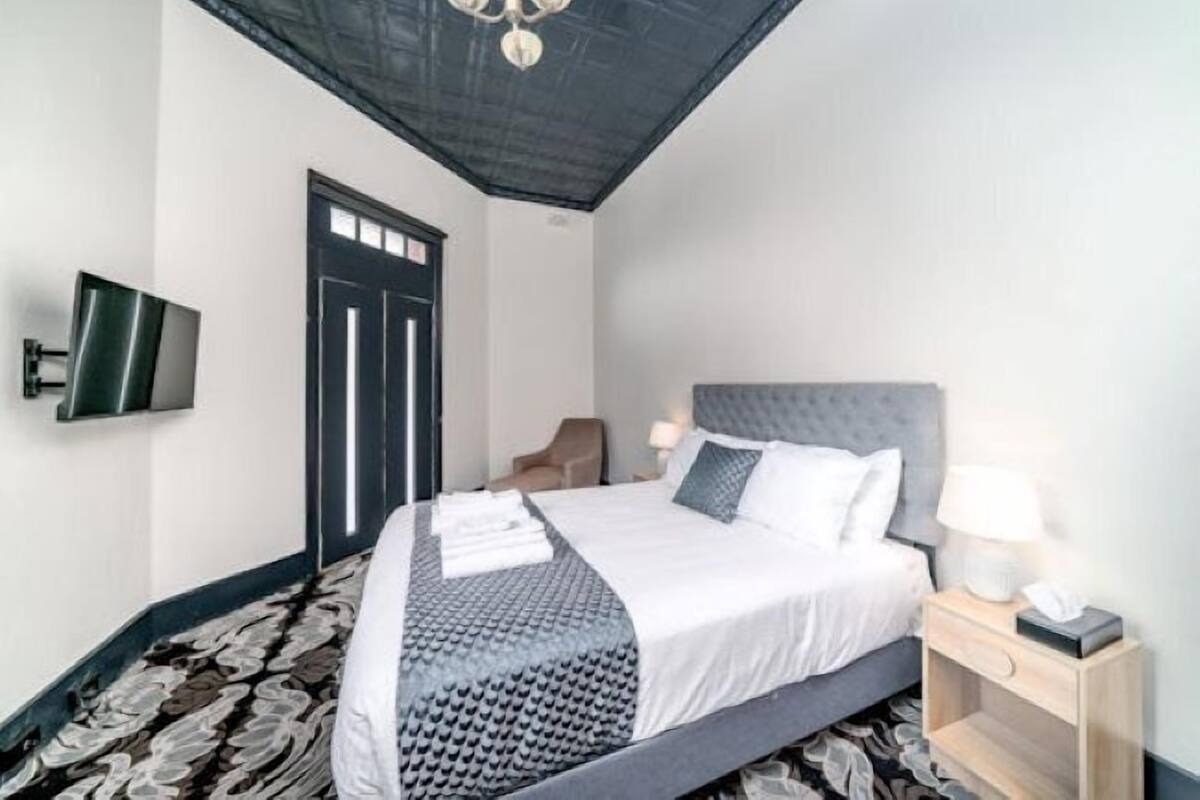 A hotel room with a bed, bedside table, lamp, and a television mounted on the wall.