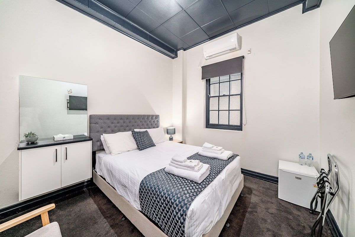 A neatly arranged bedroom with a bed, bedside table, wardrobe, and a small desk with a chair.
