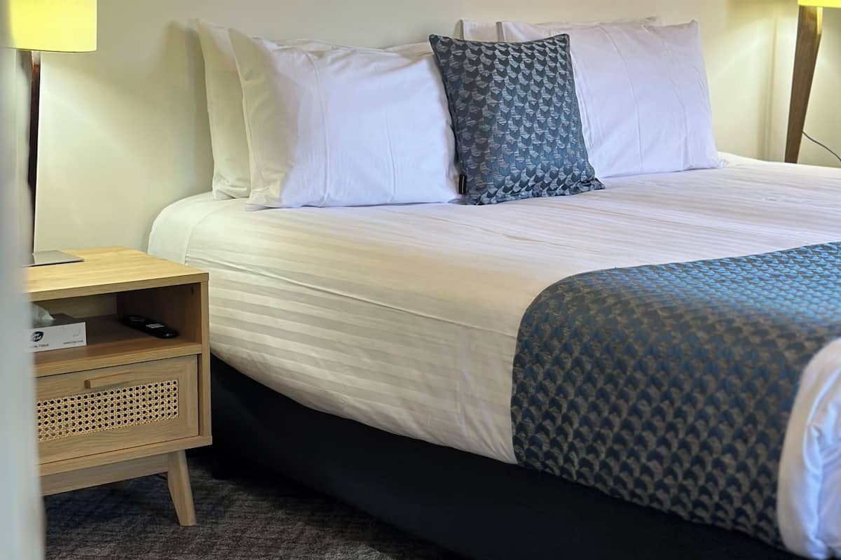 A hotel room with a bed, bedside lamps, a nightstand, a chair, and a carpeted floor.