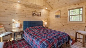 Une pièce de cabane en bois comprenant un lit, une chaise, une table de chevet et une fenêtre.