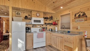 Une cuisine rustique aménagée dans une cabane en bois, comprenant un réfrigérateur, une cuisinière, un four à micro-ondes et des placards en bois.