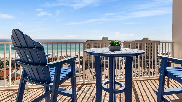 Een balkon met twee Adirondack stoelen en een kleine tafel, met uitzicht op een strand en de oceaan.