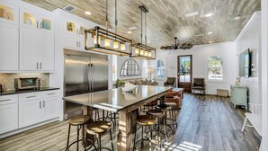 Una cocina amplia con una isla grande, taburetes de bar y un refrigerador moderno de acero inoxidable.