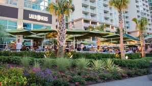 A hotel with outdoor seating areas, palm trees, and a sign for 'Lager Heads'. - Four Sails - Oceanfront & City View Balconies! (Virginia Beach)