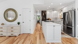 Una cocina moderna con armarios blancos, un refrigerador de acero inoxidable grande y piso de madera.