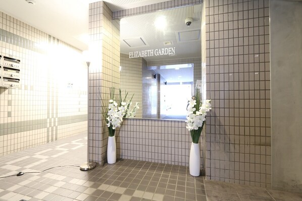 A reception area with a tiled floor and walls, a sign reading "ELIZABETH GARDEN", and two white vases with flowers.