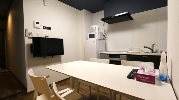 A compact kitchen with a white table, chairs, a microwave, a refrigerator, and a sink.