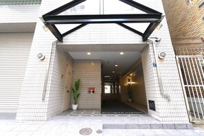 A building entrance with tiled walls, a black metal frame, and a potted plant.