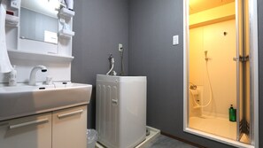 A bathroom with a white sink, a mirror, a towel dispenser, and a shower area with a glass door.