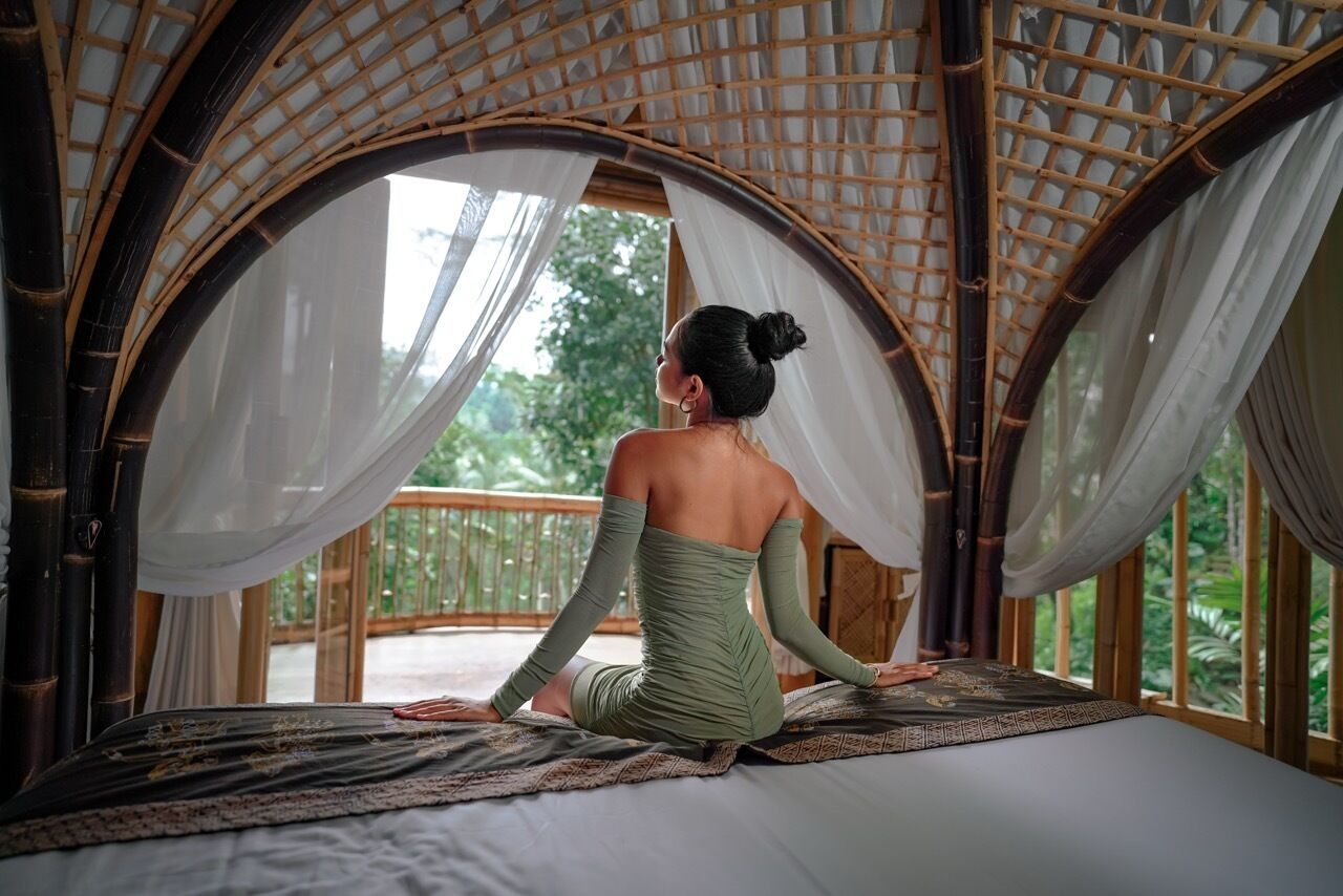 A room with a bed, a large window, and a view of greenery outside.