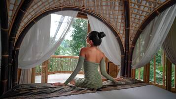 A room with a bed, a large window, and a view of greenery outside.