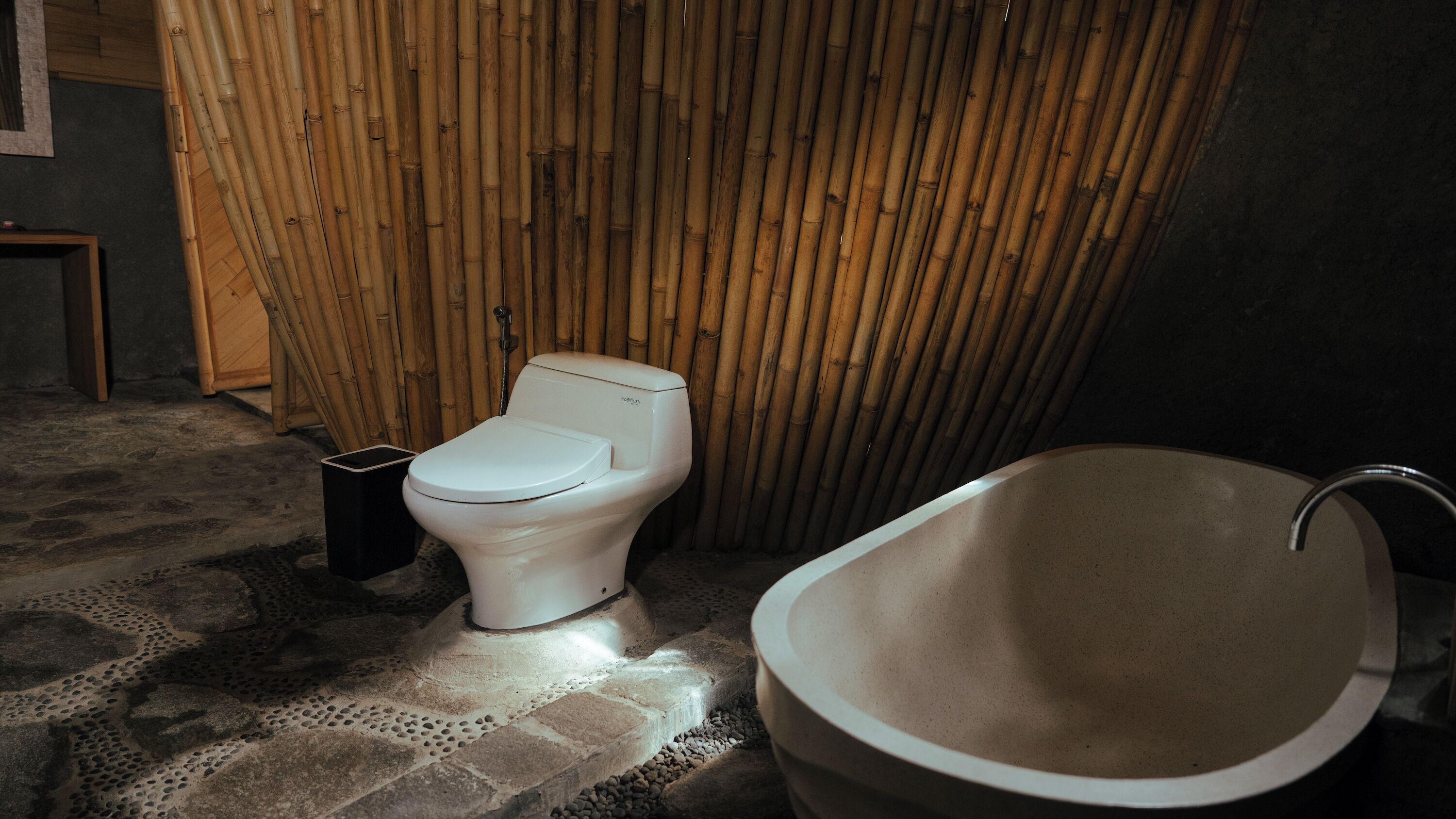 A bathroom with a toilet, a bathtub, and a bamboo wall.