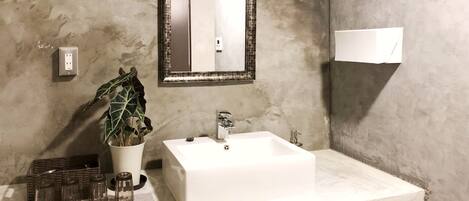 Un baño con un lavamanos blanco, un espejo con un marco decorativo, una planta en maceta y una lámpara de pared.