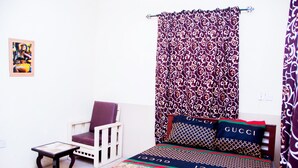 Une chambre avec des rideaux à motifs, un lit agrémenté d’oreillers de marque, une petite table et une chaise.