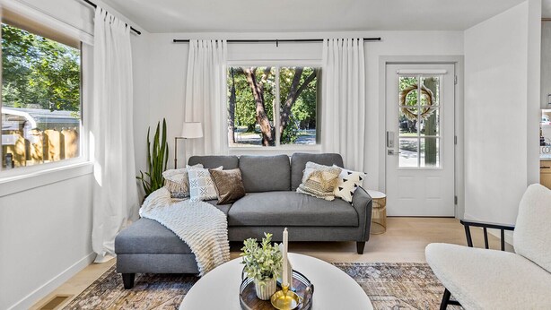A modern living room with a grey sofa, a white coffee table, and a view of trees through large windows.