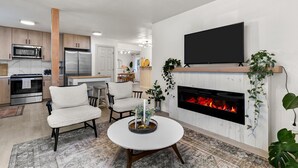 A modern living room with a fireplace, a flat-screen TV, and a dining area with a round table.
