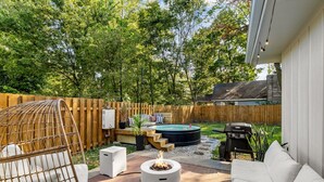 A backyard with a fire pit, outdoor seating, a hot tub, and a wooden fence.