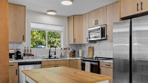 A modern kitchen with wooden cabinets, a stainless steel refrigerator, a microwave, and a wooden dining table.