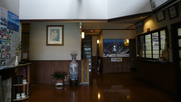 Eine Lobby mit einem hölzernen Empfangstresen, einer großen Vase und einem gerahmten Bild an der Wand.