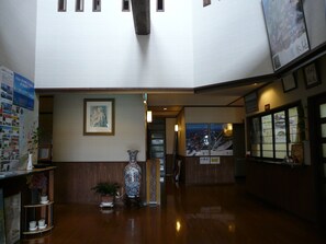 A lobby with a wooden reception desk, a large vase, and a framed picture on the wall.