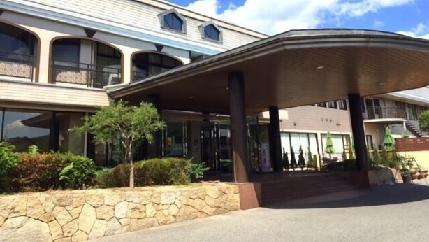 A hotel entrance with a covered walkway, stone wall, and multiple windows. - Hotel Daikoen (Takehara)