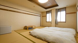Un dormitorio de estilo japonés tradicional con suelo de tatami, futón, una pequeña mesa de madera y un radiador blanco.