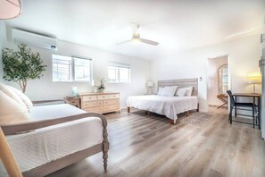 A bedroom with two beds, a dresser, a desk, and a ceiling fan.